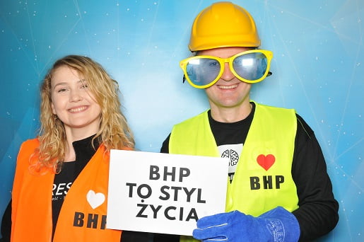 Uśmiechnięci mężczyzna i kobieta w kamizelkach bhp stoją w fotobudce - dni bezpieczeństwa Proresult
